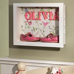 there are pink shoes in the shadow box on the wall above the crib that is decorated with flowers and birds