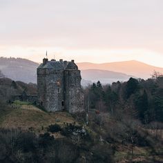 an old castle sitting on top of a hill next to trees and hills in the background