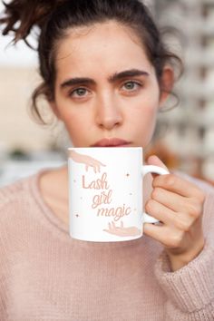 a woman holding a coffee mug with the words lashes girl magic on it in front of her face