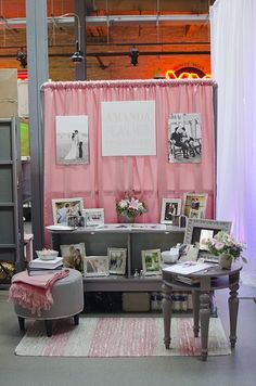 a display with pictures and photos on the wall next to a chair in front of a pink curtain