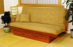 a wooden futon bed sitting on top of a hard wood floor next to a potted plant