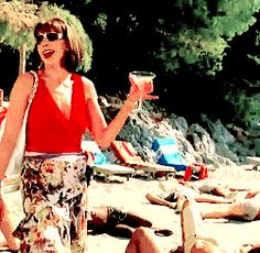 a woman standing on top of a sandy beach holding a glass of wine and an umbrella