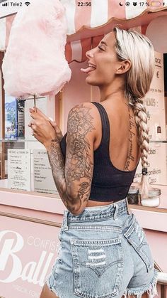 a woman holding a cotton candy lollipop in front of a pink ice cream stand