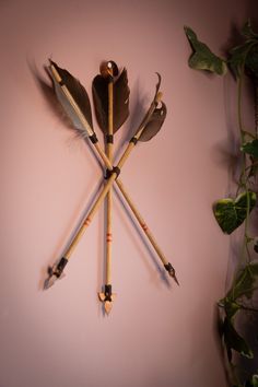 a clock made out of wooden sticks with arrows and feathers on the face, against a pink wall