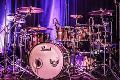 a drum set is shown in front of a blue curtain and purple lighting behind it