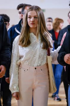 a woman in white shirt and pants walking with other people