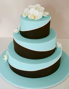 a three tiered cake with flowers on the top is blue and has black stripes