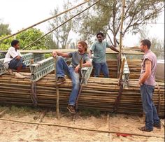 three men sitting on top of a boat made out of bamboo sticks and wood planks