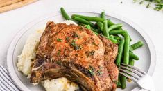 a white plate topped with meat, mashed potatoes and green beans next to a fork