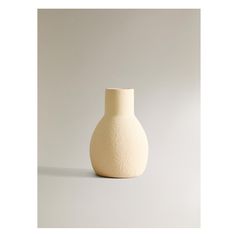 a white vase sitting on top of a table next to a gray wall and floor