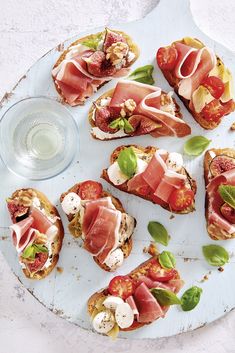 several slices of bread topped with meat and veggies next to a glass of water