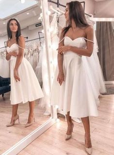 a woman standing in front of a mirror wearing a white dress