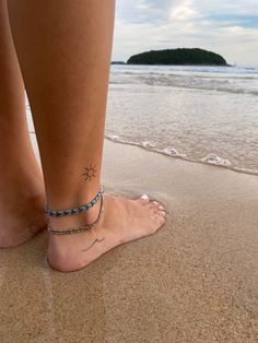 a woman's foot with a star tattoo on it, standing in the sand at the beach