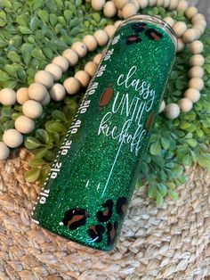 a close up of a bottle on a table with beads and plants in the background