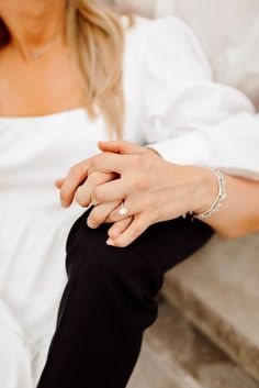 a woman in white shirt and black pants sitting on steps with her hands clasped together