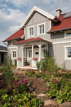 a house with red roof and white trim on the front porch, surrounded by flowers and greenery