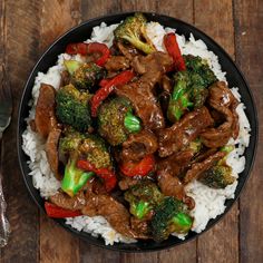 beef and broccoli stir fry on rice in a black bowl next to a fork