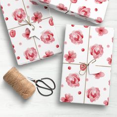 three wrapped gifts with pink flowers on them next to twine and spools of twine