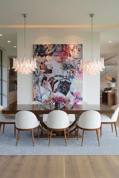 a dining room table with white chairs and a large painting on the wall behind it