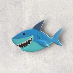 a blue plastic shark with teeth on it's back and mouth open, sitting on concrete