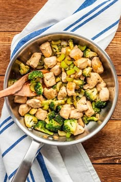 a pan filled with chicken and broccoli on top of a blue and white towel