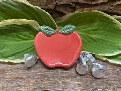 a red apple sitting on top of a wooden table next to green leaves and silver coins