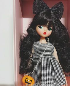 a doll with long black hair in a pink box holding a jack - o'- lantern