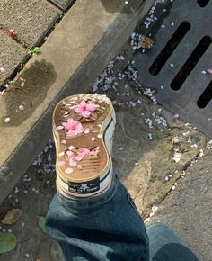 someone's foot with flowers on the ground next to a drain