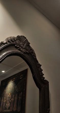 an ornate wooden mirror hanging on the wall above it's reflection, in front of a painting