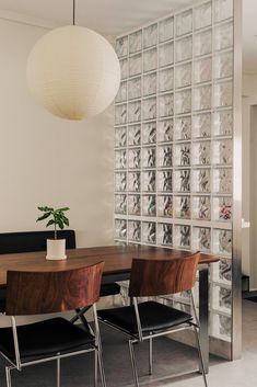 a dining room table with four chairs and a plant in the center, next to a glass block wall