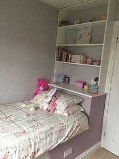 a small child's bedroom with a pink teddy bear on the bed and bookshelves