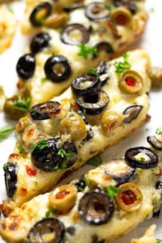 several pieces of pizza with olives and herbs on them sitting on a white surface