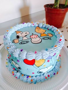 a blue cake with cartoon characters on it sitting on a plate next to a potted plant