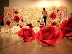 a woman standing on a ladder in front of a flower wall with red and white roses