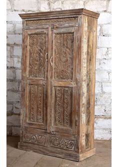 an old wooden armoire with carvings on the front and sides, against a brick wall