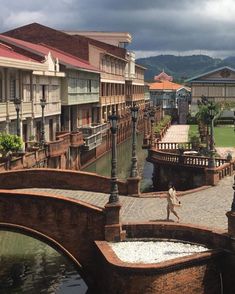 a man walking across a bridge over a river next to tall buildings with balconies on them