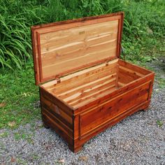 an open wooden box sitting on top of a gravel road next to green grass and bushes