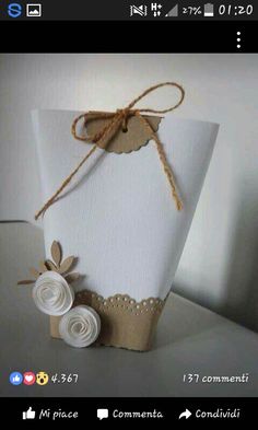 a small white box with some paper flowers on it's side and a brown string tied to the top