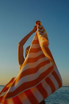 a woman is holding an orange and white striped towel over her head while standing on the beach