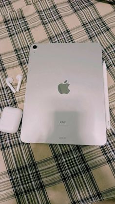 an apple computer sitting on top of a bed next to headphones and earbuds