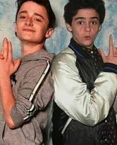 two young men standing next to each other in front of a blue background with one giving the peace sign