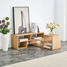 a vase with flowers sitting on top of a table next to a book shelf and guitar