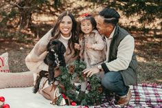 a man and woman sitting on a blanket with their dog in front of christmas decorations