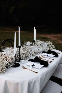 a table with white flowers and black napkins on it is set up for an outdoor dinner