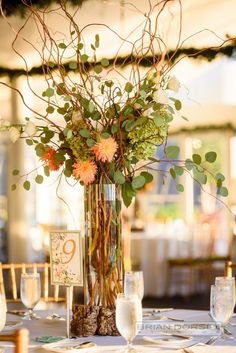 a vase filled with flowers and greenery on top of a white table cloth covered table