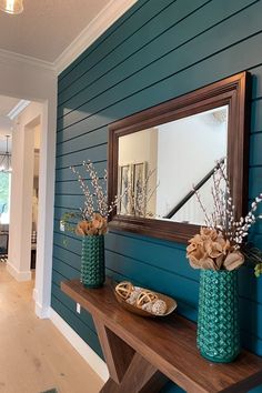 two vases filled with flowers sit on a wooden table in front of a mirror