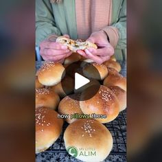 a person holding a piece of bread in front of buns on a wire rack