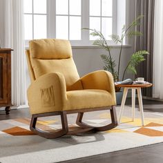 a yellow rocking chair sitting on top of a rug next to a table with a potted plant