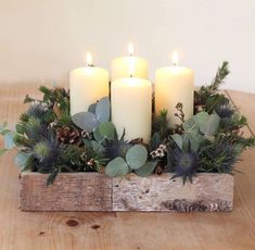 three candles are sitting in a wooden box with greenery and pine cones on it