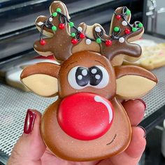 a hand holding up a cookie shaped like a reindeer's head with christmas decorations on it